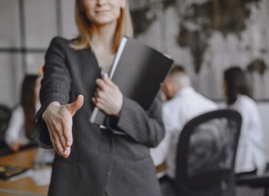 Woman in a suit holds a folder. Girl signs the documents. Lady sitting on the table. Manager working in the office.